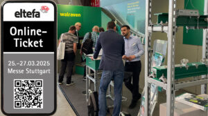 Der Walraven Messestand auf der Elektromesse eltefa 2025. Zu sehen ist Standpersonal, ein paar Besucher, sowie eine Freikarte auf einem Smartphone am linken Bildrand. Im Hintergrund ist eine grüne Walraven-Wand zu sehen.