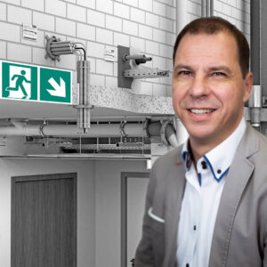 Webinar zur brandgeprüften Befestigung: Referent Tobias Weber vor einer technischen Darstellung von Befestigungs- und Brandschutzsystemen in einem Gebäude.