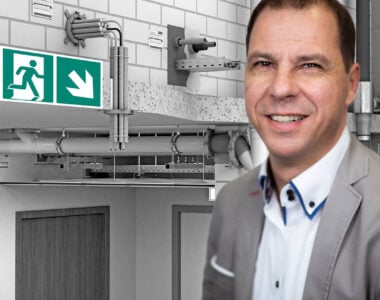 Webinar zur brandgeprüften Befestigung: Referent Tobias Weber vor einer technischen Darstellung von Befestigungs- und Brandschutzsystemen in einem Gebäude.