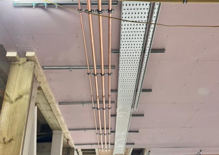 Parallel geführte Kupferrohre unter der Decke, befestigt mit Rohrschellen an Walraven RapidRail® Montageschienen neben einer Kabeltrasse.