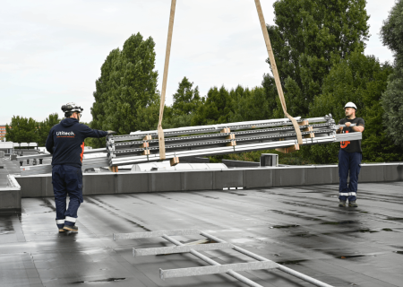 Zwei Utitech Monteure positionieren per Kran vorgefertigte Walraven RapidStrut® Bauteile auf dem Flachdach beim TLR Projekt.