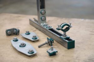 Produktanordnung des RapidStrut Montageschienensystems mit Montageschiene, Verbindungselementen und Hammerfix auf einer Werkbank. Das Bild zeigt die modularen Komponenten zur sicheren Befestigung und flexiblen Montage von Rohrleitungen und technischen Installationen.